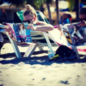 A woman on the beach is reading a fashion magazine